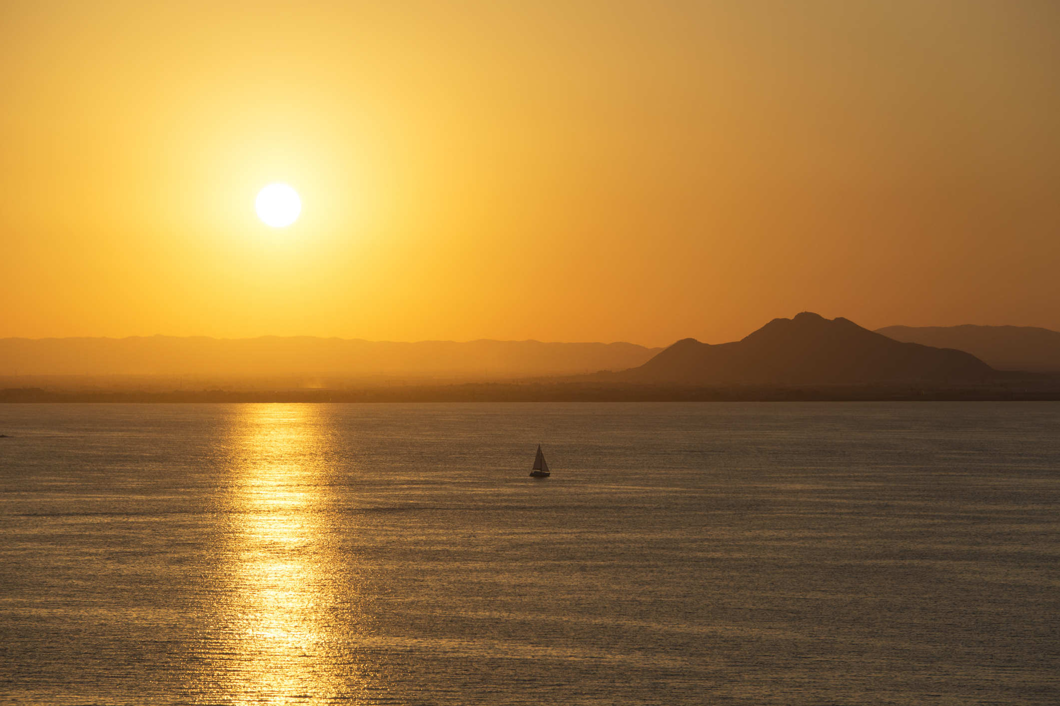 Pequeña embarcación navegando frente al horizonte montañoso al atardecer – La Manga, lado del Mar Menor, Cabo de Palos, Cartagena y San Javier, Murcia, España, Europa.